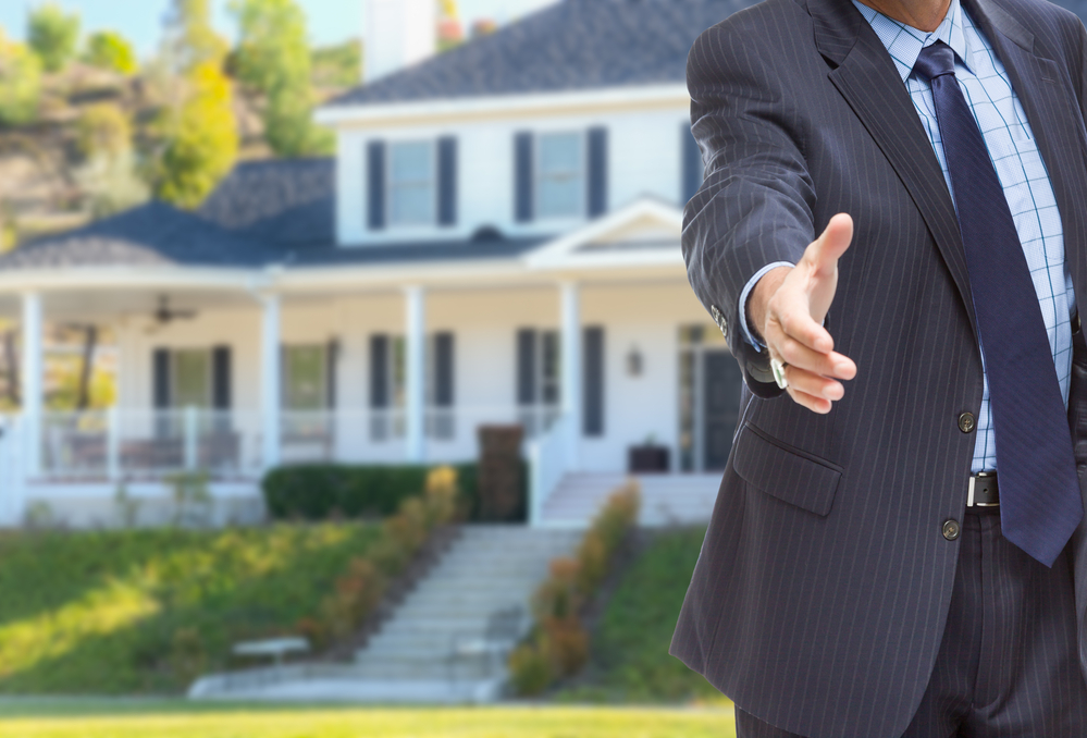 male agent reaching for hand shake in front of beautiful new house.
