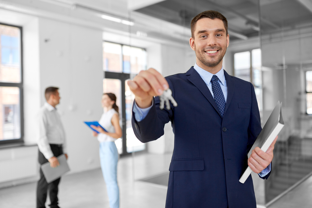 smiling realtor with keys and folder at new office