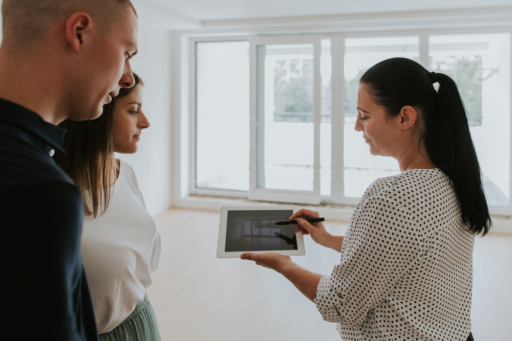 estate agent using digital tablet showing young couple new house.